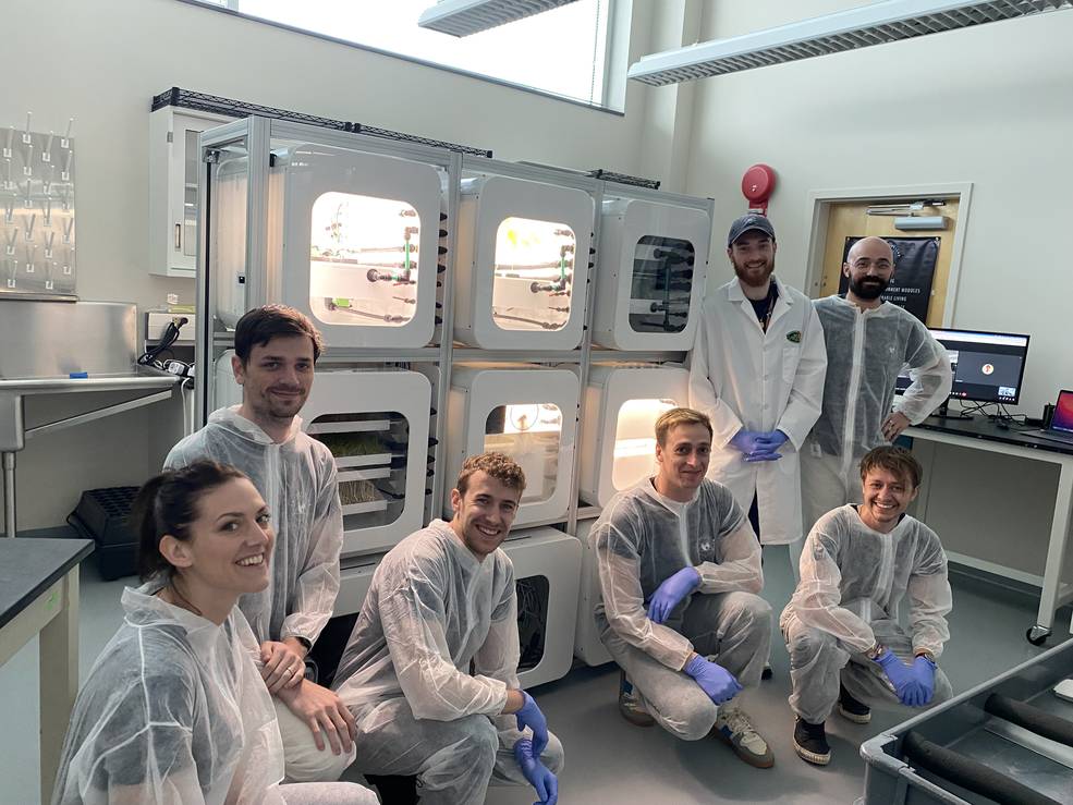 The Interstellar Lab team of seven people gather in lab coats in front of the NUCLEUS system. 