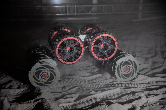 With the lights out, the ISRU Pilot Excavator (IPEx) breadboard unit, also known as RASSOR, digs in the regolith bin during testing inside Swamp Works at Kennedy Space Center.
