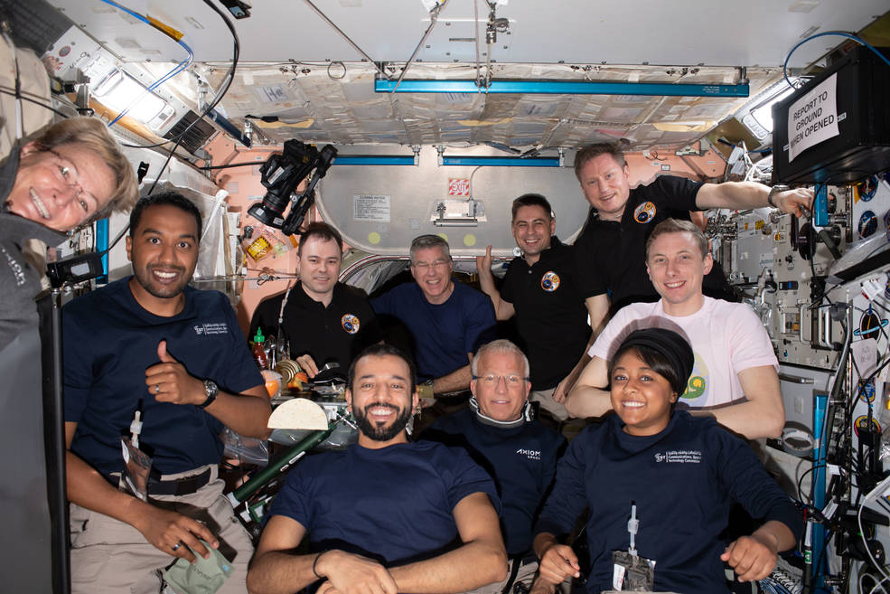 The Axiom Mission-2 and Expedition 69 crew members pose for a portrait together during dinner time aboard the International Space Station.