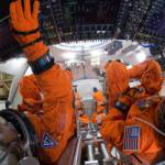 Engineers in orange spacesuits sit inside a mockup of the Orion spacecraft.