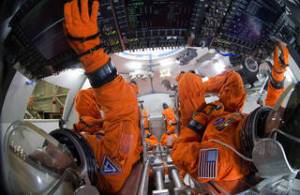 Engineers in orange spacesuits sit inside a mockup of the Orion spacecraft.