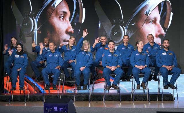 Graduating astronauts sit in chairs on stage during their graduation ceremony