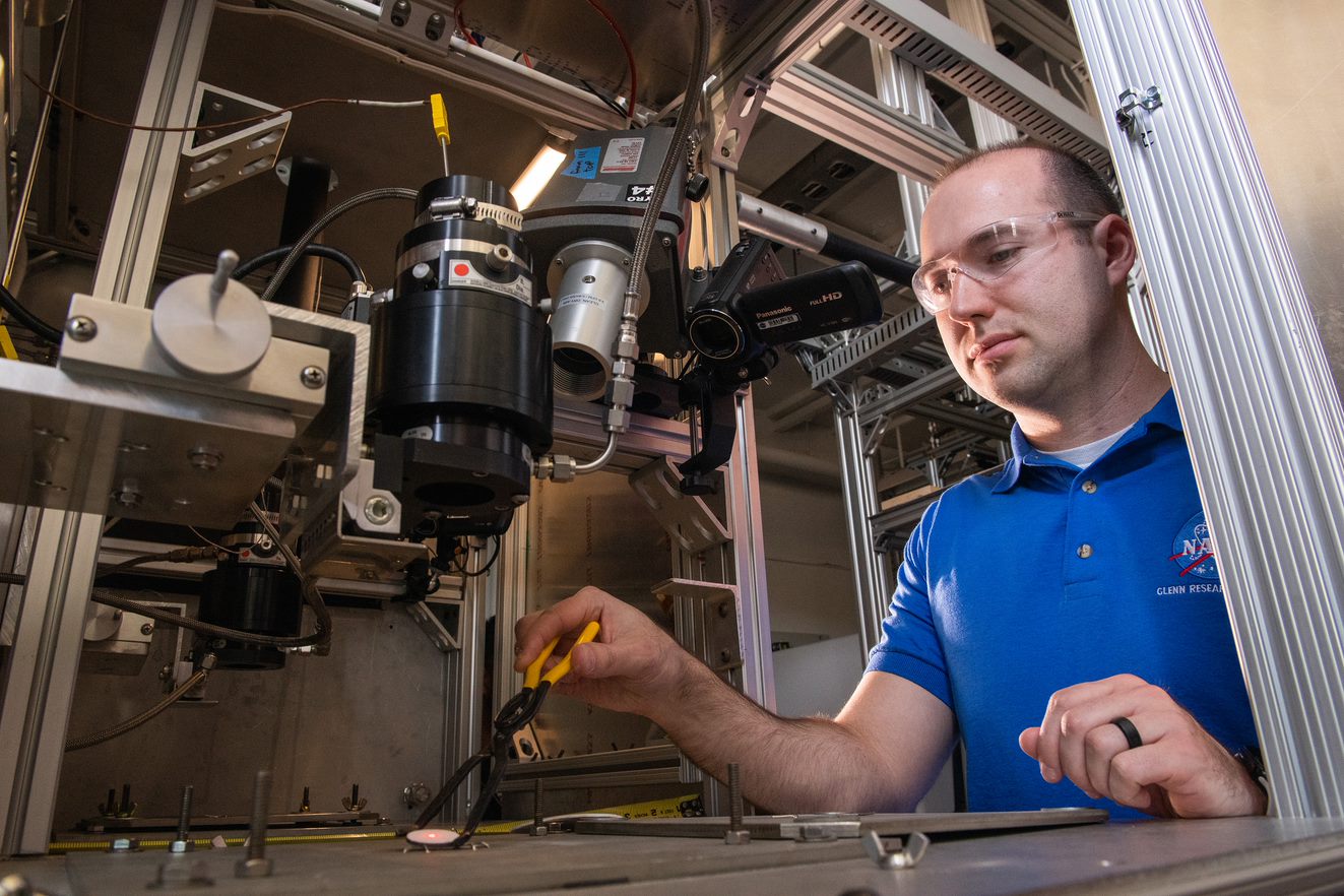 A man in a blue shirt, installing an environmental barrier coated ceramic matrix composite sample.