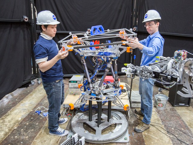These two NASA robots, with assistance from engineers Iok Wong and Kyle Doyle, are working together to assemble pieces of a truss segment like a big Erector set.