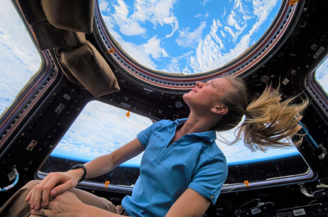 NASA astronaut Karen Nyberg, Expedition 37 flight engineer, enjoys the view of Earth from the windows in the Cupola of the International Space Station. A blue and white part of Earth is visible through the windows.