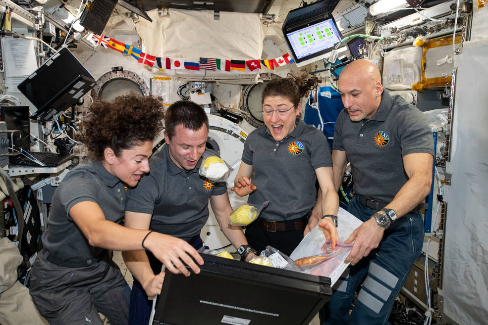 Crew members aboard the International Space Station unpack newly delivered fresh fruit and other goodies in October 2019. From left are NASA flight engineers Jessica Meir, Andrew Morgan, and Christina Koch with ESA Commander Luca Parmitano.