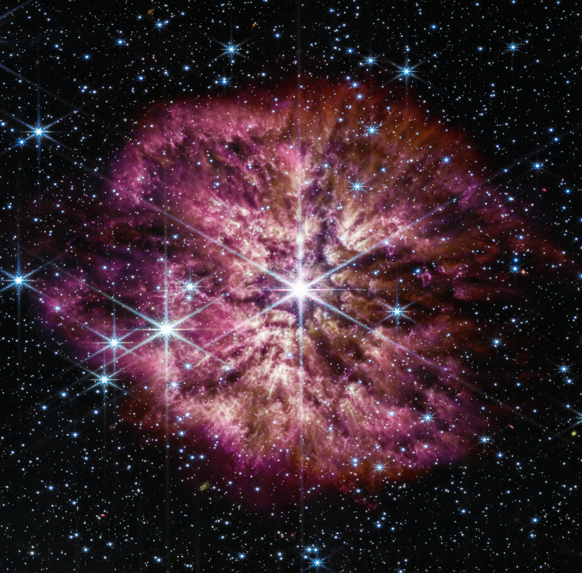 A large, bright star shines from the center with smaller stars scattered throughout the image. A clumpy cloud of material surrounds the central star, with more material above and below than on the sides.