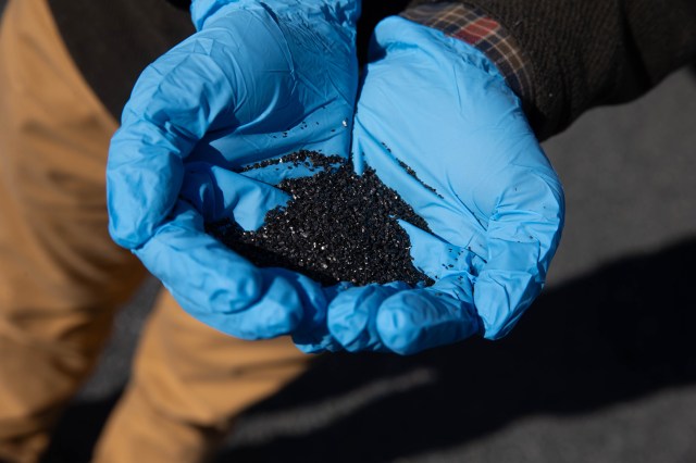 A pair of hands wearing blue gloves cupped together holding granules of carbon.