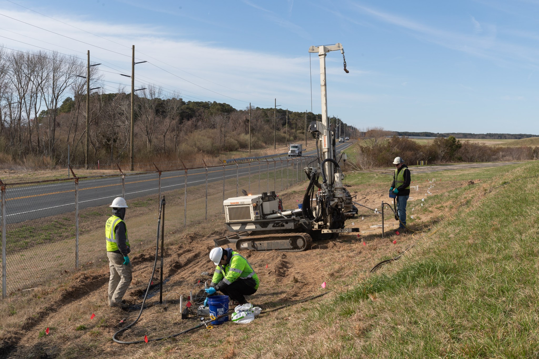 A group of technicians in hard hats and high-visibility vests drilling into a grassy field.