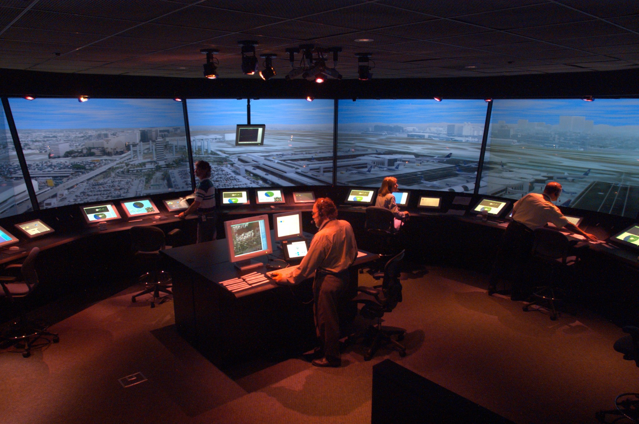 A simulator of an air traffic control tower, with large monitors showing an airport and cityscape in the background.