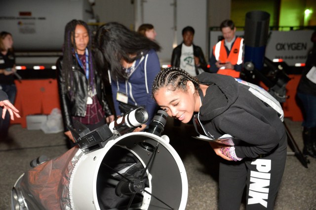 A young black girl looks through a telescope.