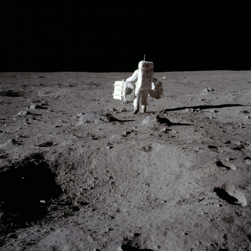 Apollo 11 astronaut Buzz Aldrin carries experiment equipment on the surface of the Moon.