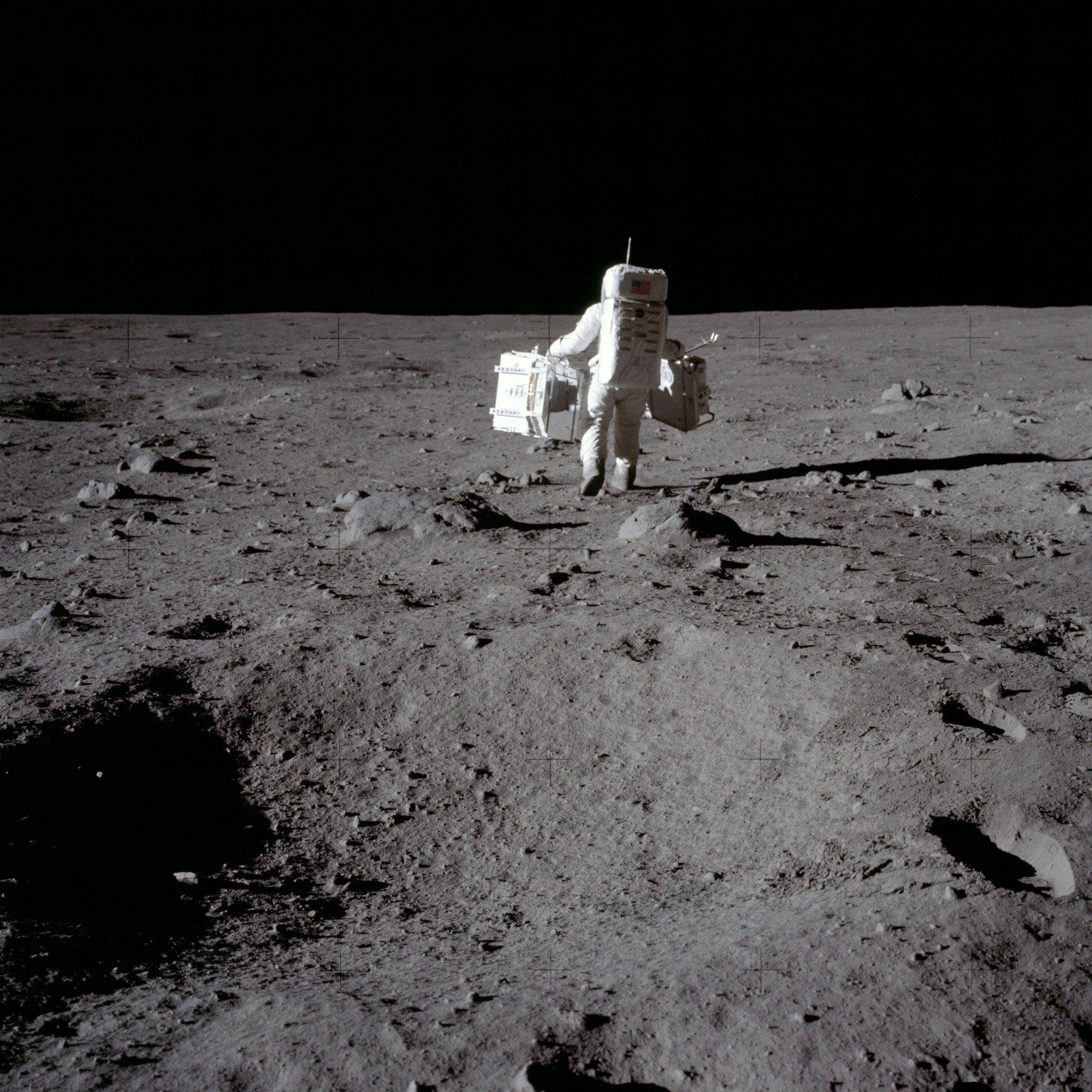 Astronaut Edwin E. Aldrin, Lunar Module (LM) pilot, carries the Passive Seismic Experiments Package (PSEP) (left) and the Laser Ranging Retroreflector (LRRR) (right), to the deployment area. These two experiments make up the Early Apollo Scientific Experiment Package (EASEP). Image taken at Tranquility Base during the Apollo 11 Mission. Original film magazine was labeled S. Film Type: Ektachrome EF SO168 color film on a 2.7-mil Estar polyester base taken with a 60mm lens. Sun angle is Medium. Tilt direction is South (S).