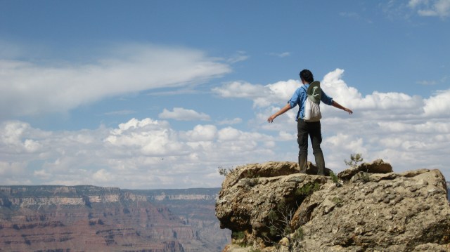 A person stands on the side of the Grand Canyon, their back to the camera and their arms spread wide.