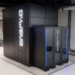 The D-Wave quantum computer, encased in black paneling with the logo for "D-Wave" illuminated on the side and the front of the unit.