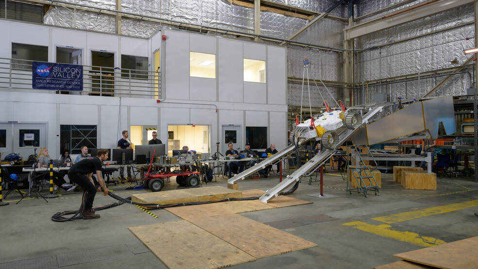 A team member adjusts the cables that power and send commands to the VIPER test unit as engineers practice its exit/descent from the model Griffin lunar lander.