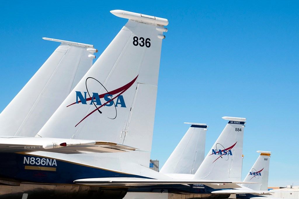 Against a clear sky, the vertical tail fins of three F-15 jets used by NASA are seen, some displaying a NASA logo.