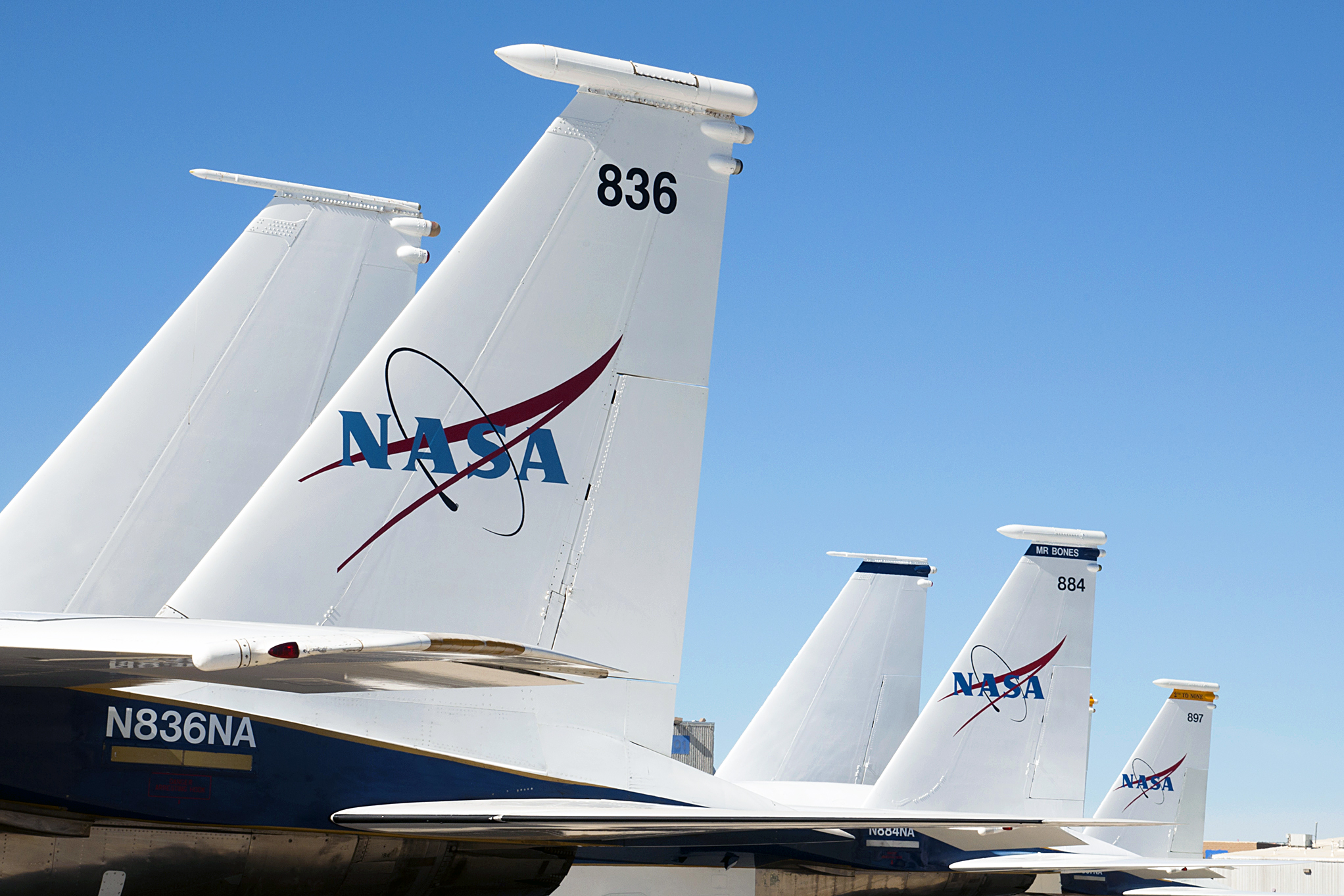 Against a clear sky, the vertical tail fins of three F-15 jets used by NASA are seen, some displaying a NASA logo.