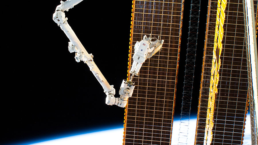 Astronaut Woody Hoburg rides the Canadarm2 robotic arm and carrying a roll-out solar array to its installation point on the space station's starboard truss structure during a spacewalk on June 15, 2023.