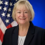 Photo of Carol Carrol with the U.S. flag behind her.