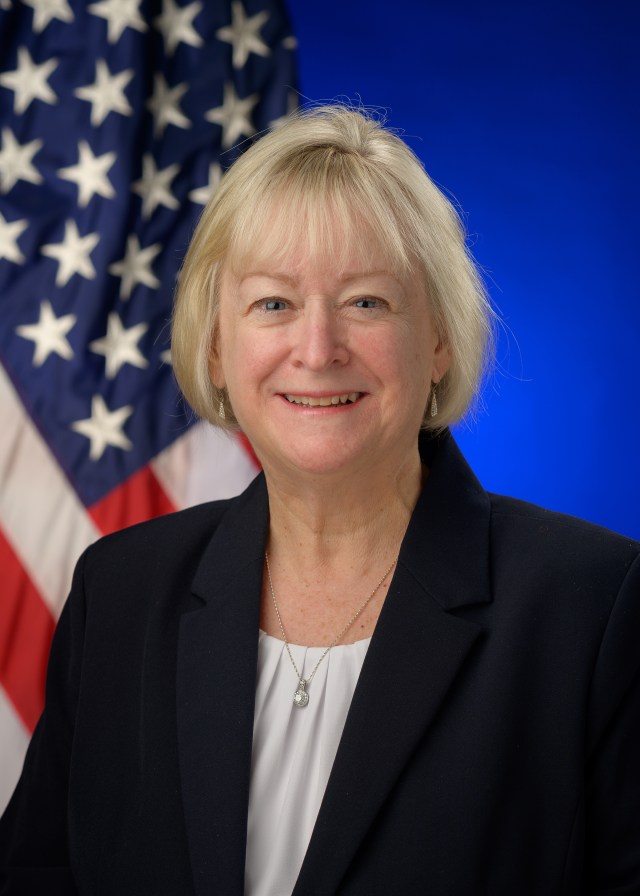 Photo of Carol Carrol with the U.S. flag behind her.