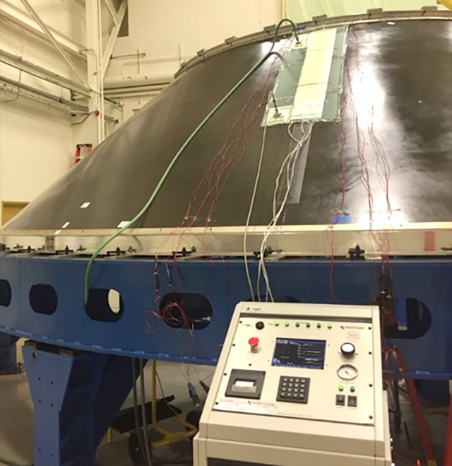 A control panel sits in front of a large payload machine.