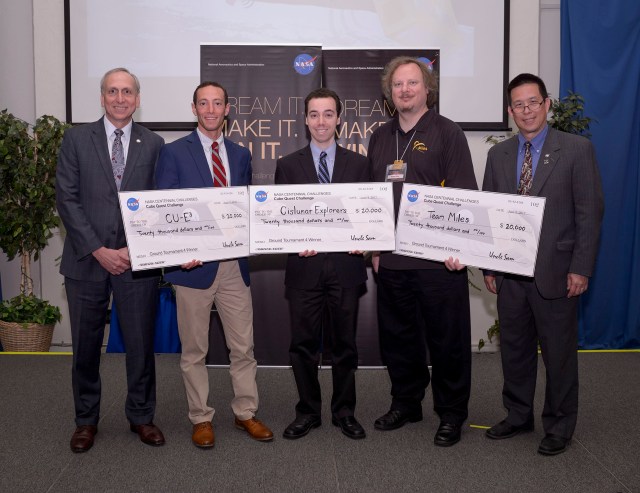 Five men stand and smile as they hold three large checks. On each check, the payer's name is NASA Centennial Challenges Cube Quest Challenge and includes an image of the NASA meatball logo. The recipient names on each check, from left to right, are CU-E3, Cislunar Explorers, and Team Miles. Each check is for $20,000 and is endorsed by Uncle Sam. The checks are dated for June 8, 2017, and the memo line reads “Ground Tournament 4 Winner” on each check.