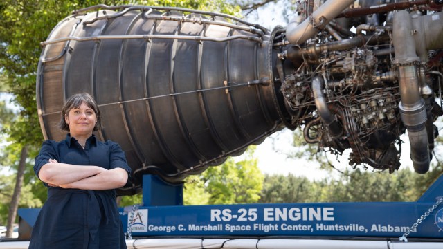 A woman with short brown hair stands in front of a RS25 Engine with her arms crossed