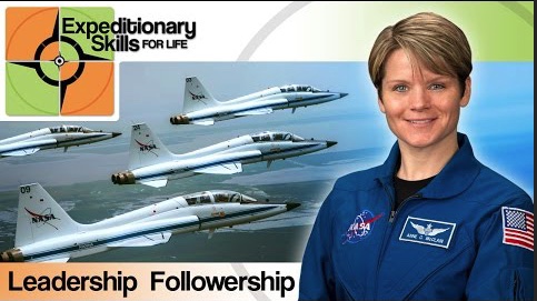 A woman in a blue astronaut jumpsuit with the words - Expeditionary Skills, Leadership Followership with four NASA jet airplanes flying in the background