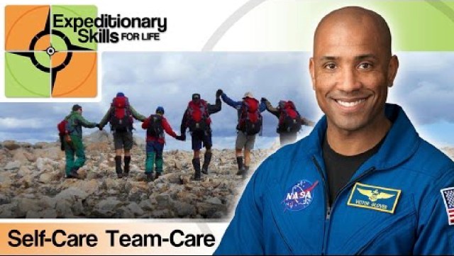 A man in a blue astronaut jumpsuit with the words - Expeditionary Skils, Team Care, Self Care