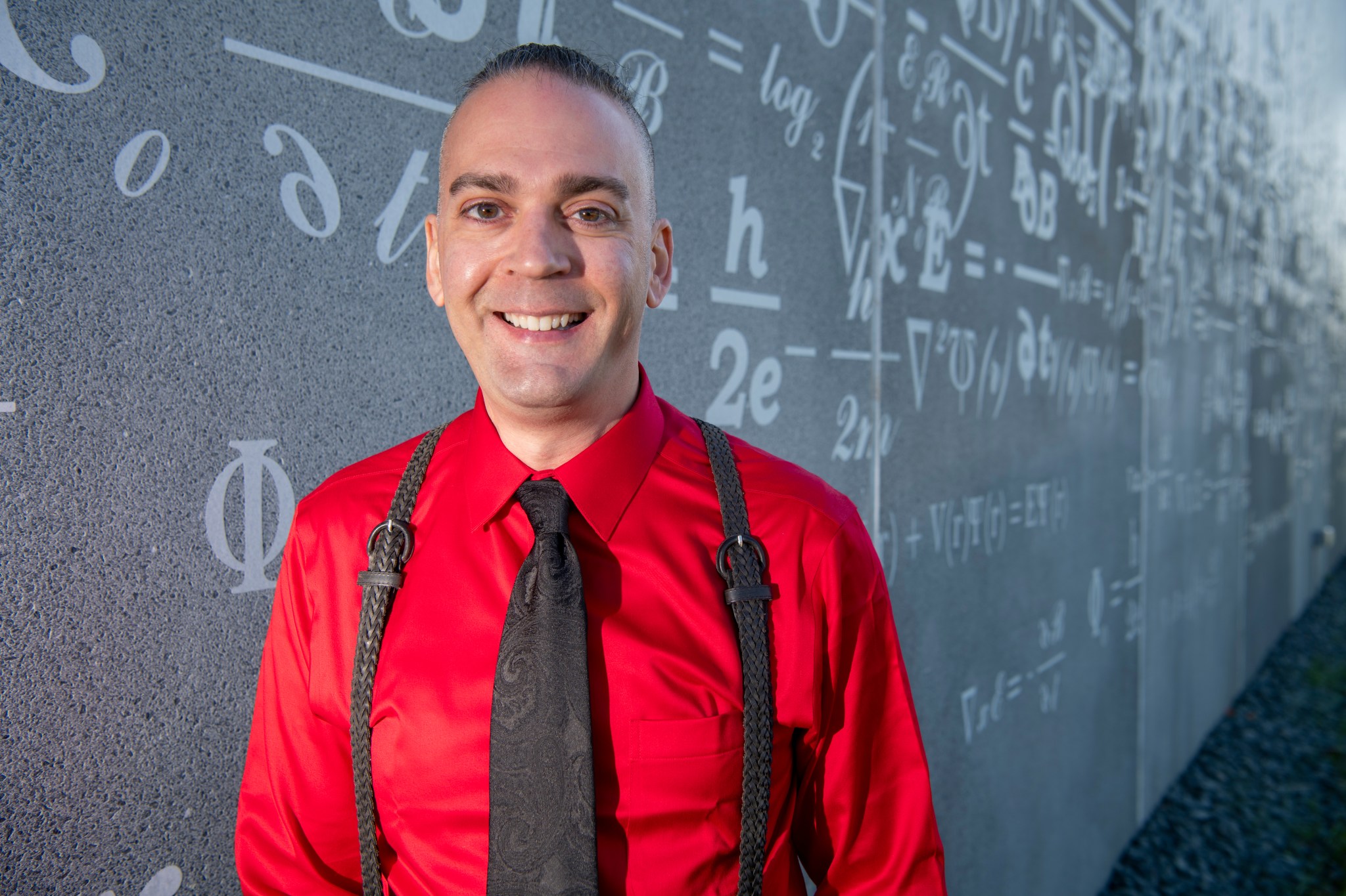 Man smiling in front of blackboard with calculations.
