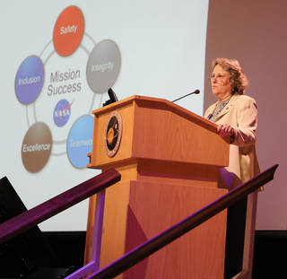DeeDee Healey speaks at a podium in the auditorium of NASA's Goddard Space Flight Center.