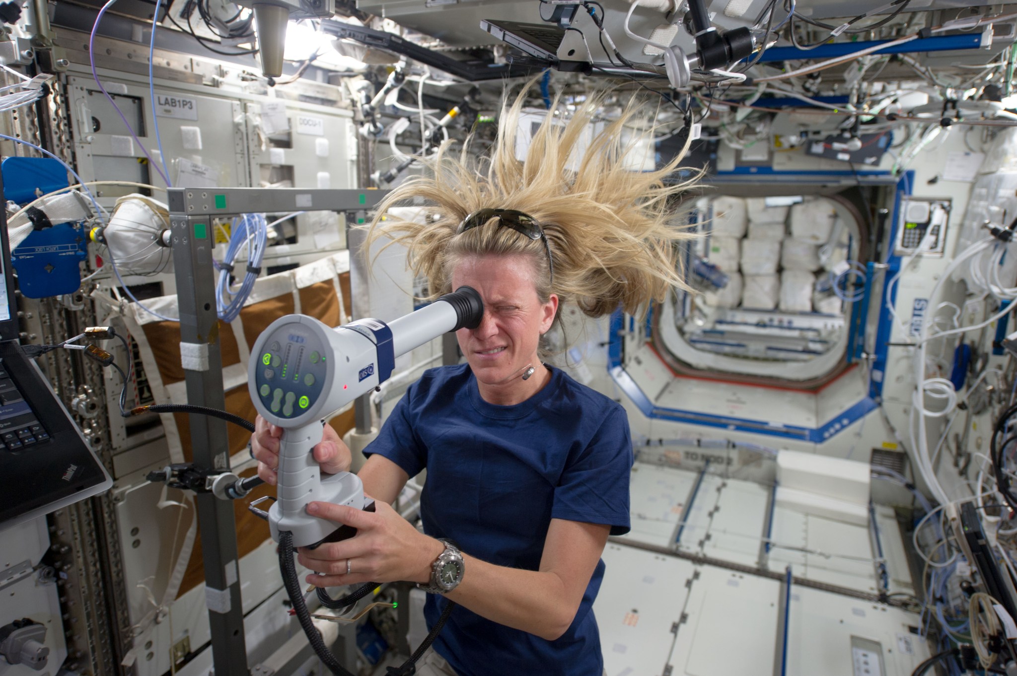 female astronaut using a fundoscope to examine her eyes while in the space station