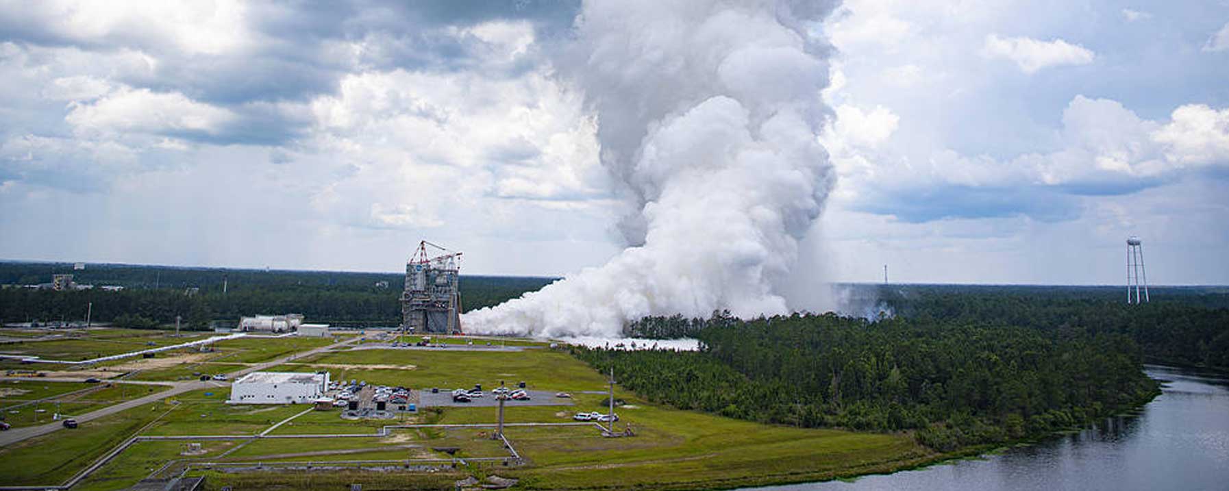 The testing stand for Stennis with smoke billowing and the river to the left of the photo.