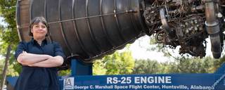 A woman stands in front of a RS-25 Engine with her arms crossed.