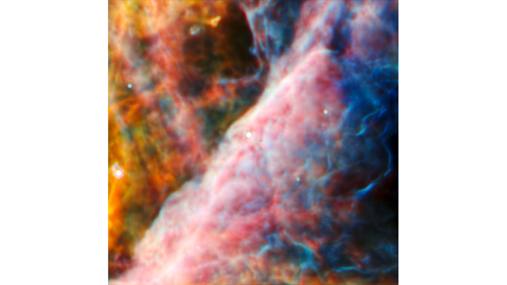 A hazy nebula of colorful material. Top left is green, red and yellow with two small stars and a darker gap region. A wall of cloudy material crosses diagonally towards the bottom right with dark blue filaments and more dark gaps in the bottom corner.