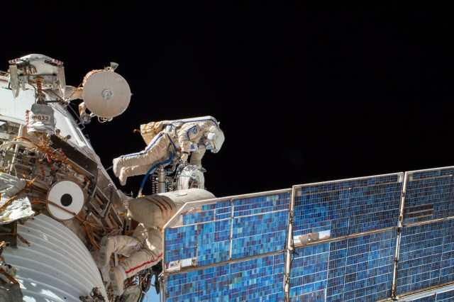 Spacewalkers in Roscosmos spacesuits exit the Poisk module's airlock attached to Zvezda.