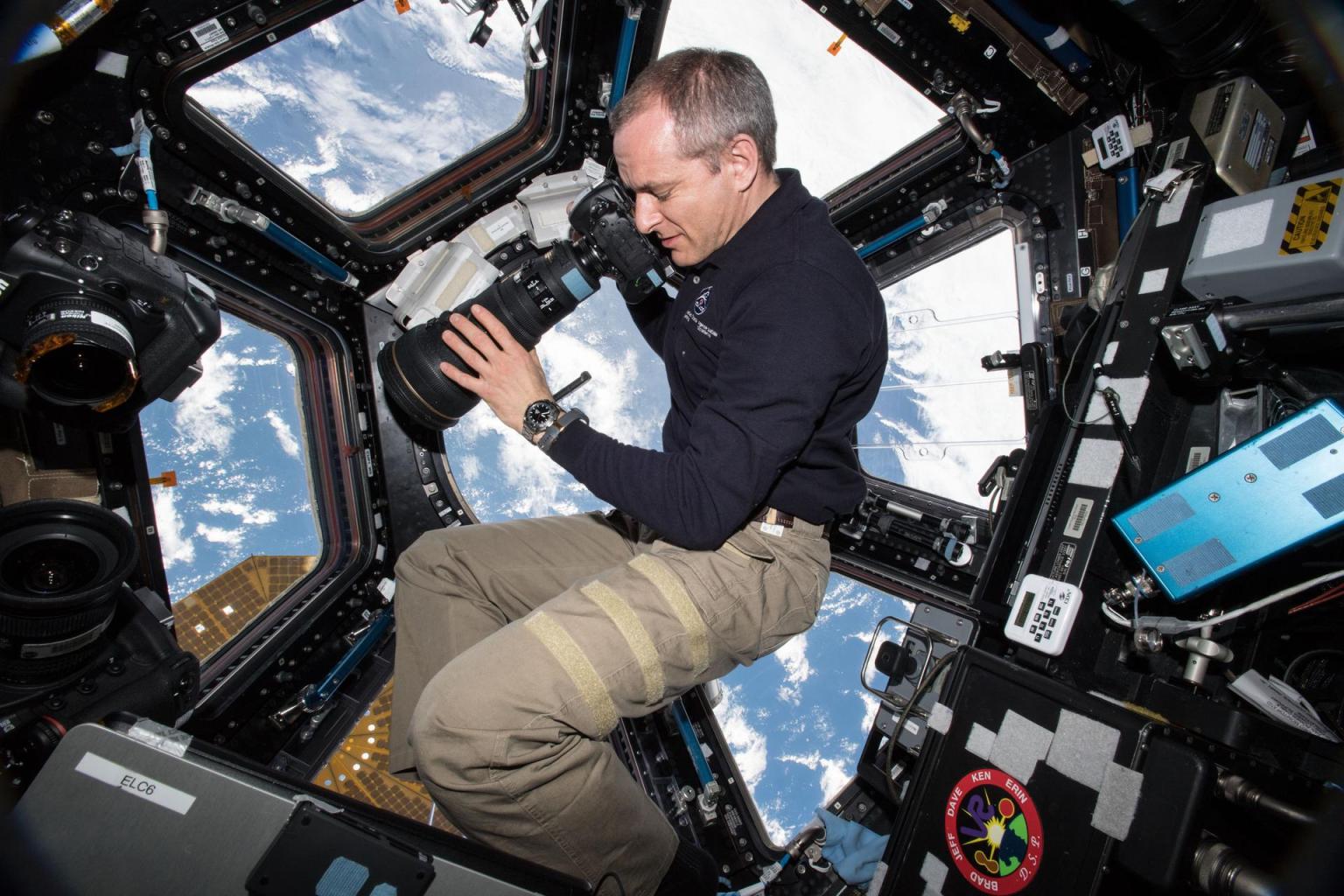 image of astronaut holding a camera taking pictures of Earth from the station's cupola