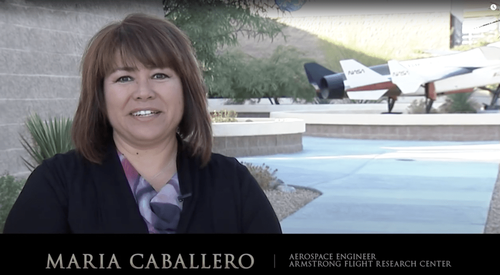 Maria Caballero standing near a building with an airplane in the background.