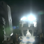 A thumbnail of the video named "NASA Prepares to Explore Moon: Spacewalks, Tools" featuring an image of an engineer wearing an exploration spacesuit walking in front of NASA's pressurized rover prototype at night during a lunar simulation test.