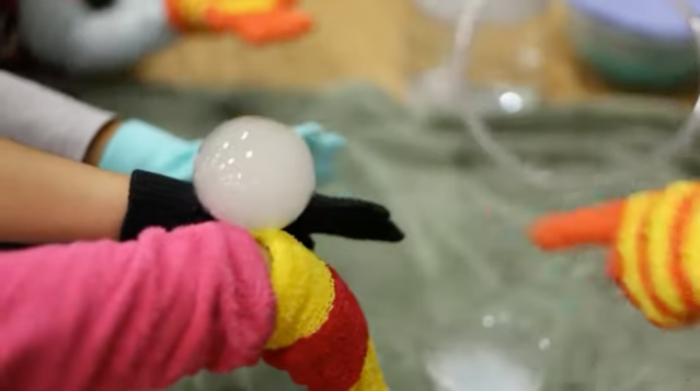 A bubble filled with smoke floats above children's hands during a Family STEM Night demonstration