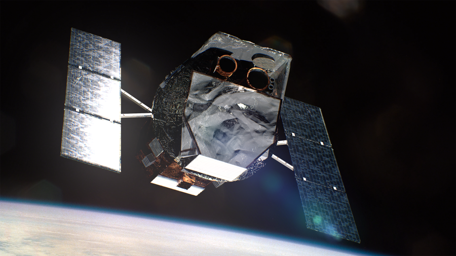 Against the blackness of space, a boxy, metallic spacecraft dominates the frame. Two "wings" of solar panels stick out from its sides. Below is the bright, cloudy limb of Earth.