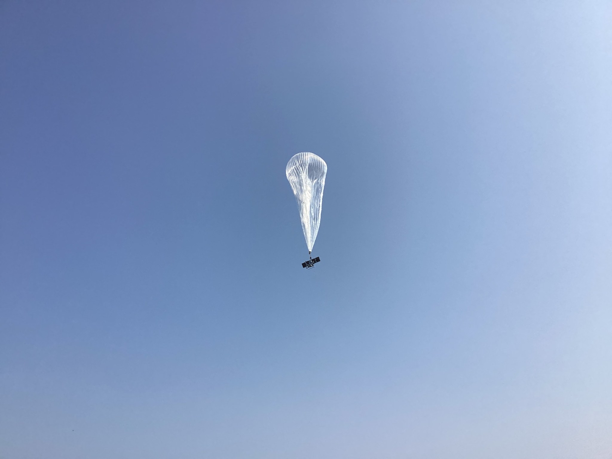 A silvery, translucent balloon with the payload gondola visible beneath it rises into the sky.