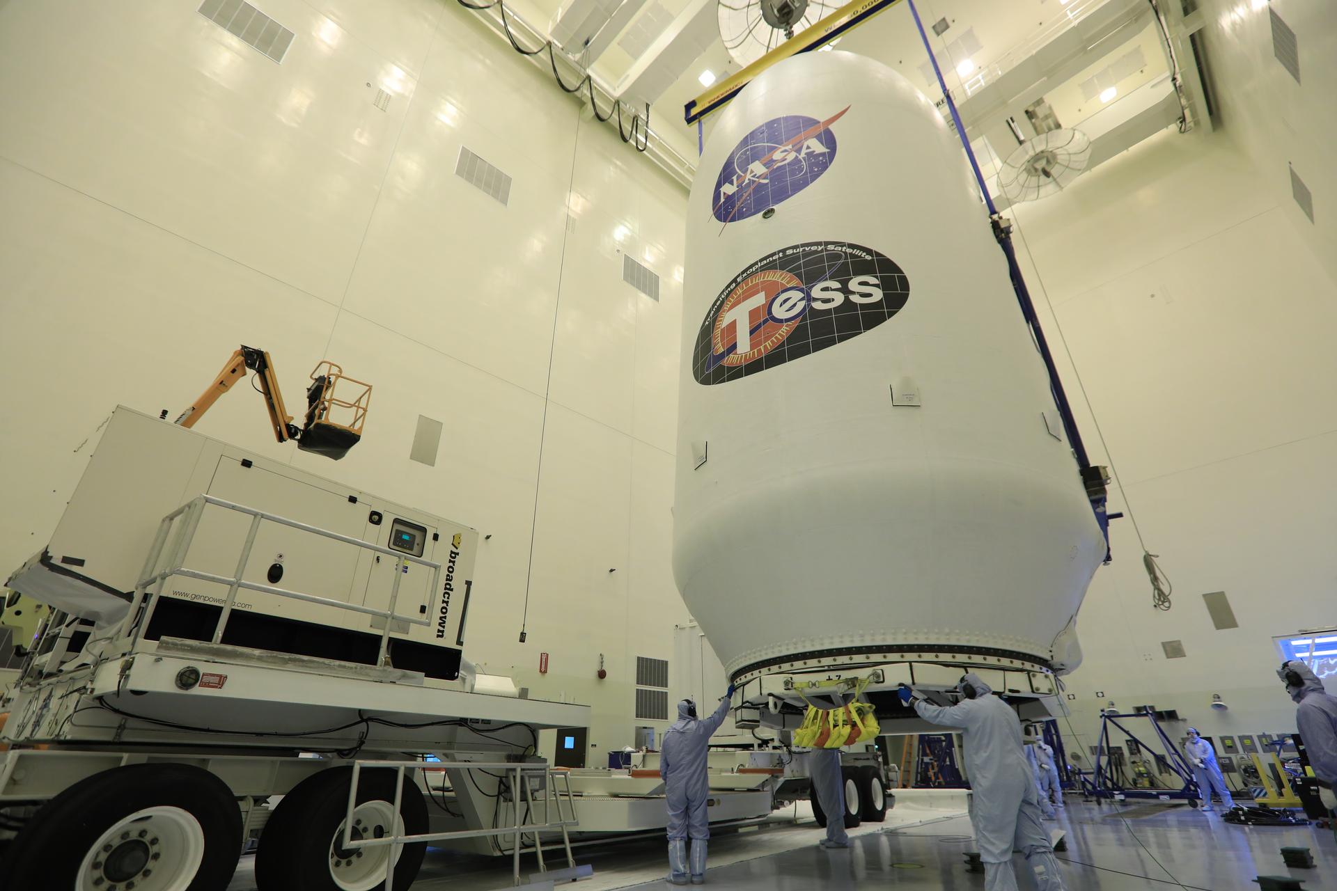 Inside the Payload Hazardous Servicing Facility at NASA's Kennedy Space Center in Florida, technicians assist as the SpaceX payload fairing containing the agency's Transiting Exoplanet Survey Satellite (TESS) is moved by crane to a transporter.