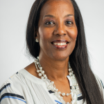 Portrait photograph of Traci Patton. A photograph of a woman with long straight dark hair smiling at the camera against a white backdrop.