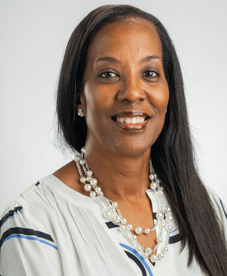 Portrait photograph of Traci Patton. A photograph of a woman with long straight dark hair smiling at the camera against a white backdrop.