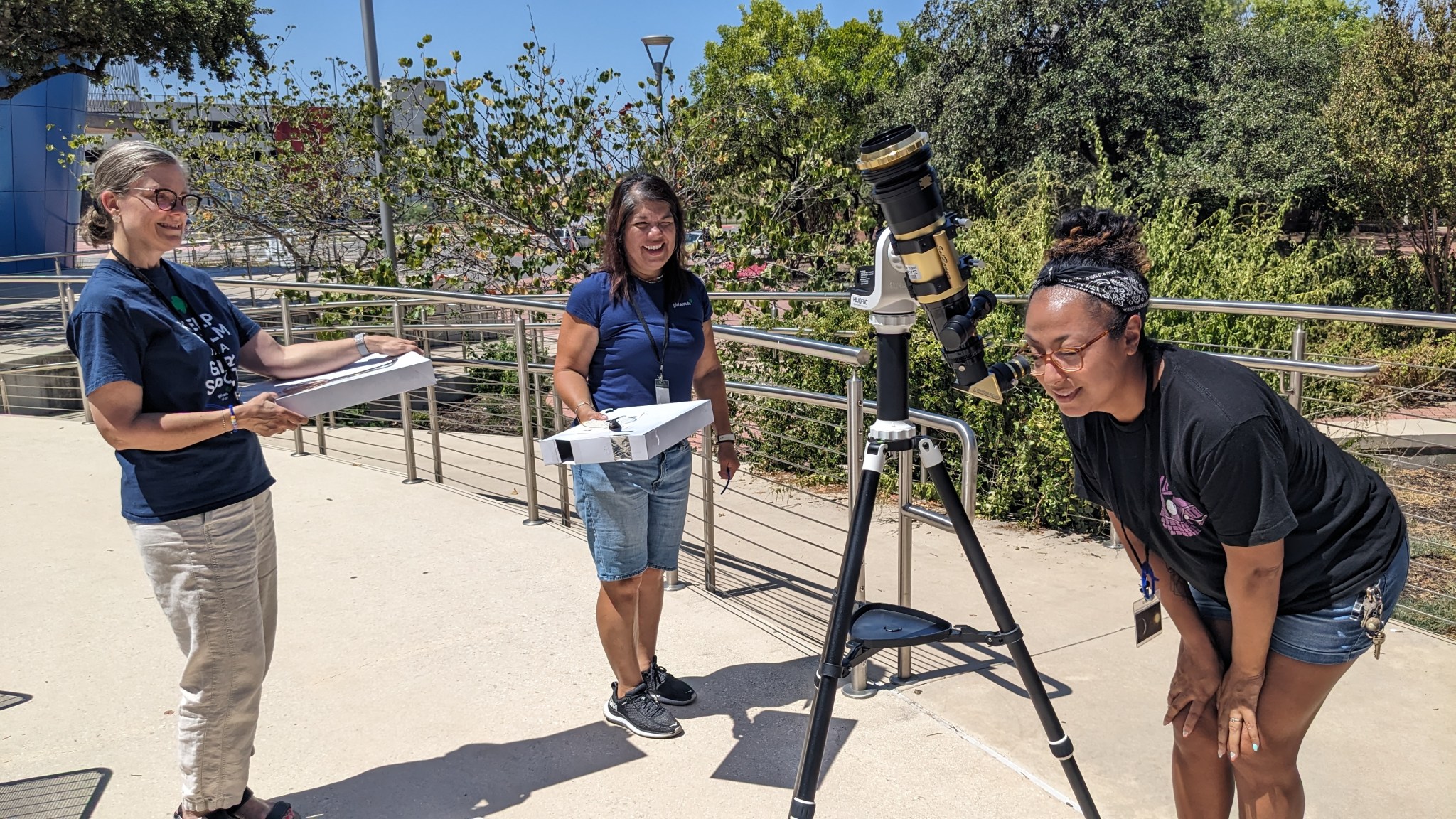 Two people watch as a third looks into a telescope