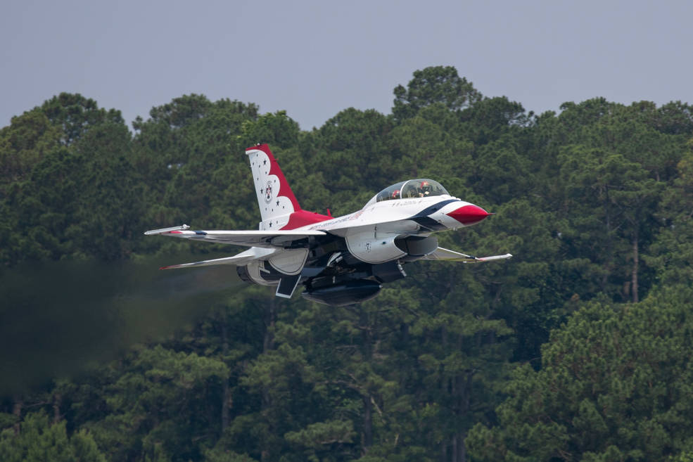 A Thunderbird F-16 jet takes off from an runway. The Thunderbirds are mostly white, with a red tip and blues stripes.