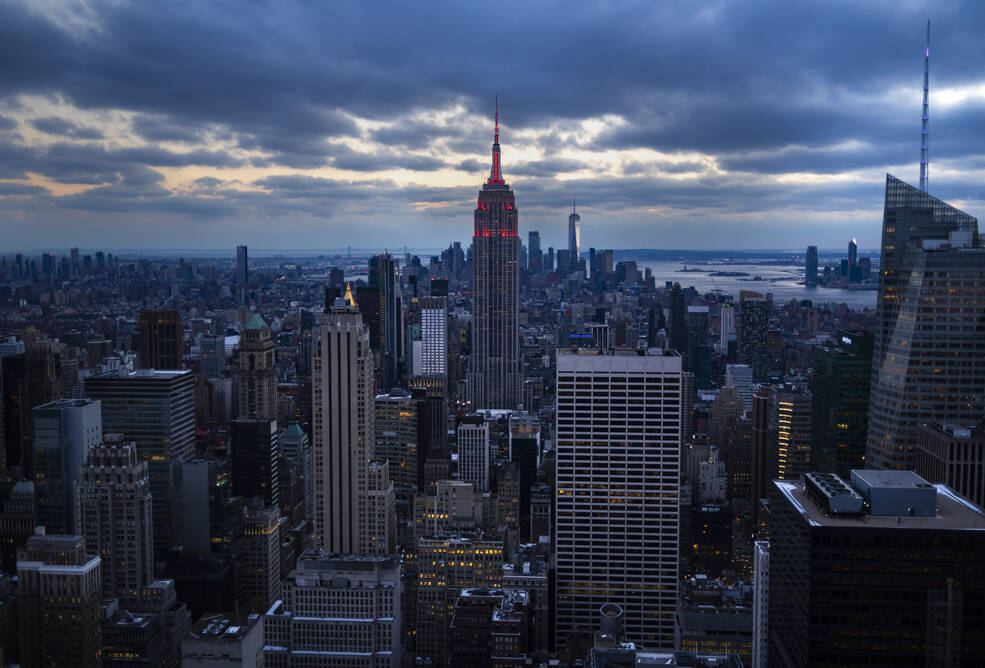 A cityscape crowded with towering skyscrapers stretches beneath blue-gray clouds at twilight.