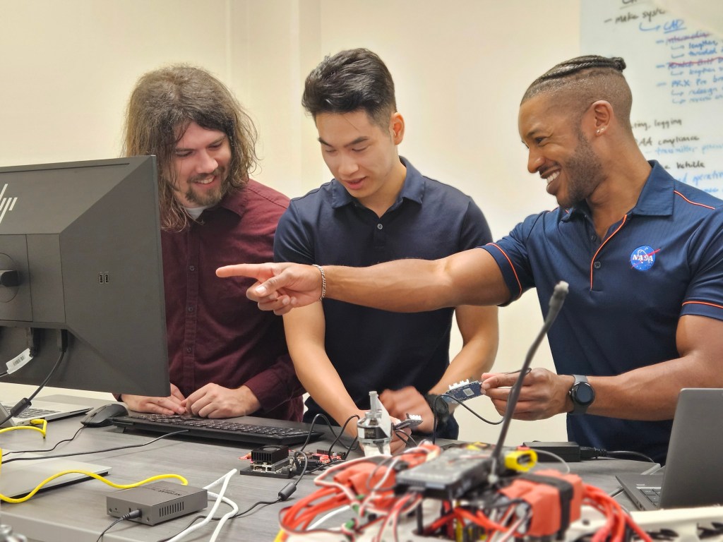 Three young men working on a small device for test and simulation.